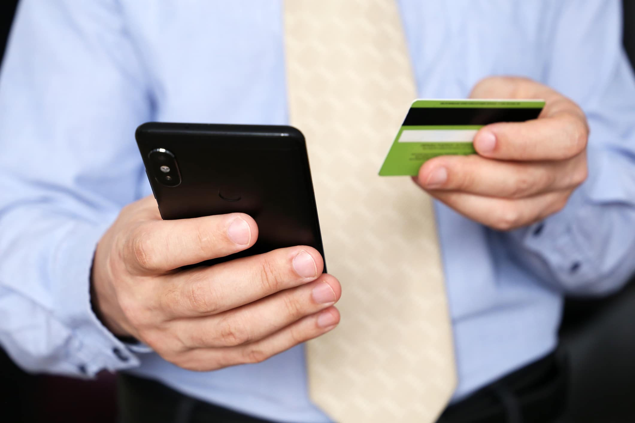 Man in office clothes holding credit bank card and smartphone in hands
